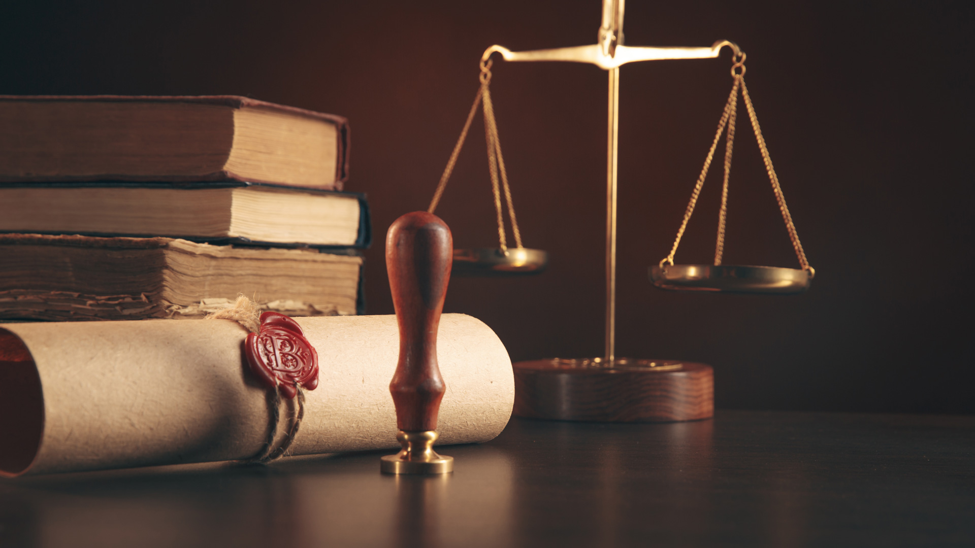 Juristisches Stillleben mit Gesetzbüchern, Siegel, Hammer und Waage vor dunklem Hintergrund.